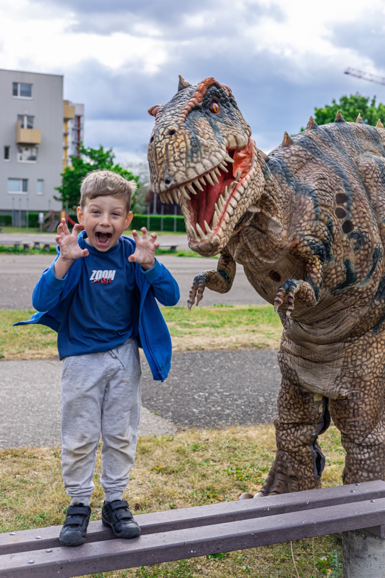 Chlapec napodobuje dinosaura a směje se, vedle něj stojí tyranosaurus